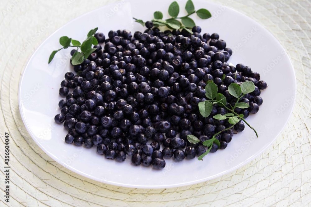 A white plate with blueberries stands on a gray wooden background.Side view A white plate with blueberries stands on a gray wooden background.Side view