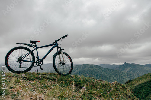 Горный велосипед на вершине горы, в дали видны горы и облака . 