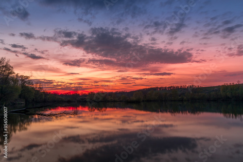 Themed sunset on a pond with a reflection of dark clouds and an orange-red glow.