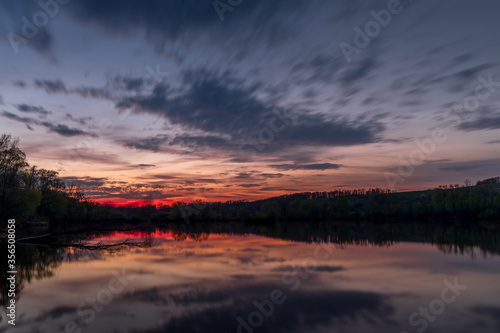 Themed sunset on a pond with a reflection of dark clouds and an orange-red glow.