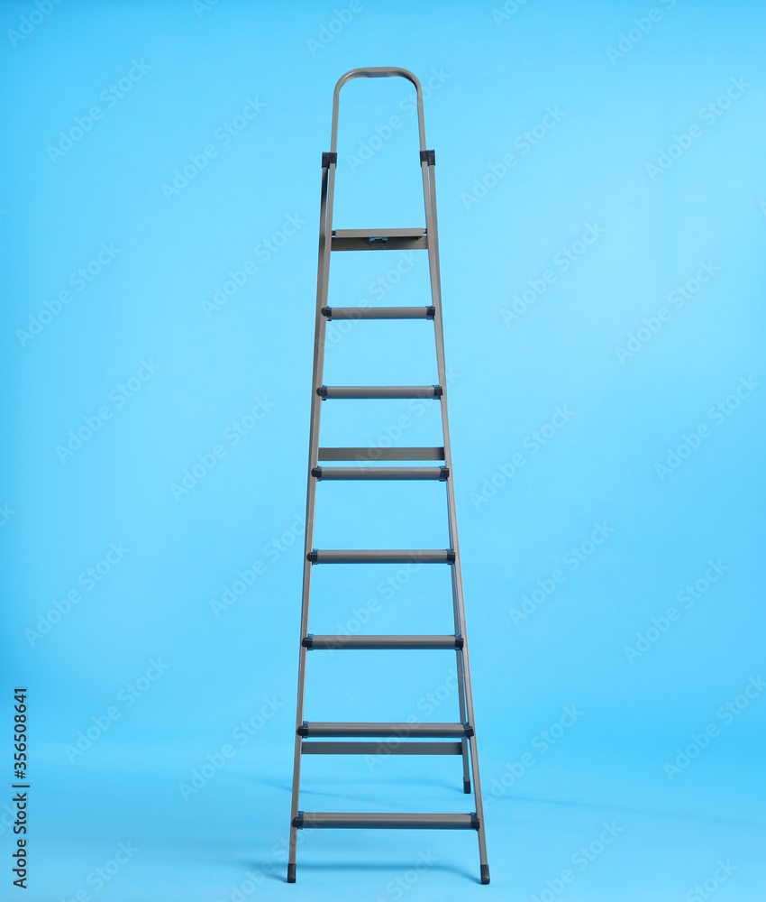 Metal stepladder on light blue background. Space for text