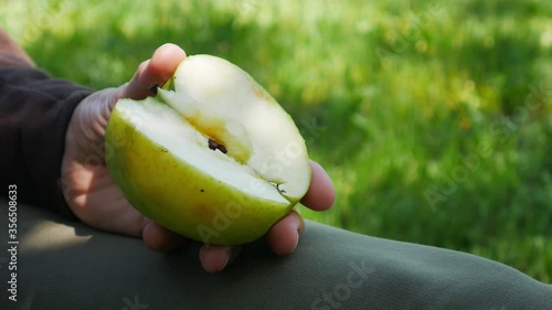 An apple cut in half in the hand of an elderly woman sitting in the garden.