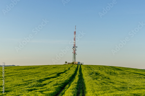 View of a broadcasting tower lying on a hill in the middle of a landscape in a field on a hill.