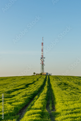 View of a broadcasting tower lying on a hill in the middle of a landscape in a field on a hill.