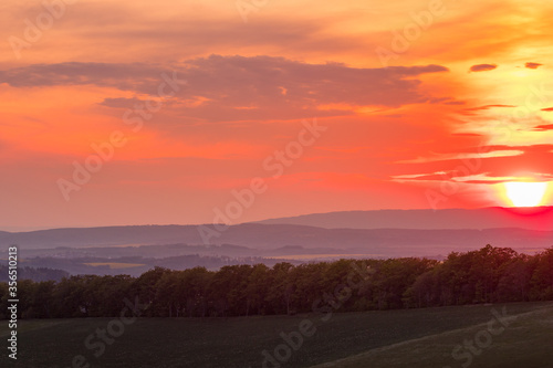 The setting sun over the forested mountain landscape of the Beskydy region, the sun sets beyond the horizon. © Lukas
