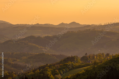 Sunrise over the mountain area covered with fog orange rays penetrate the landscape.