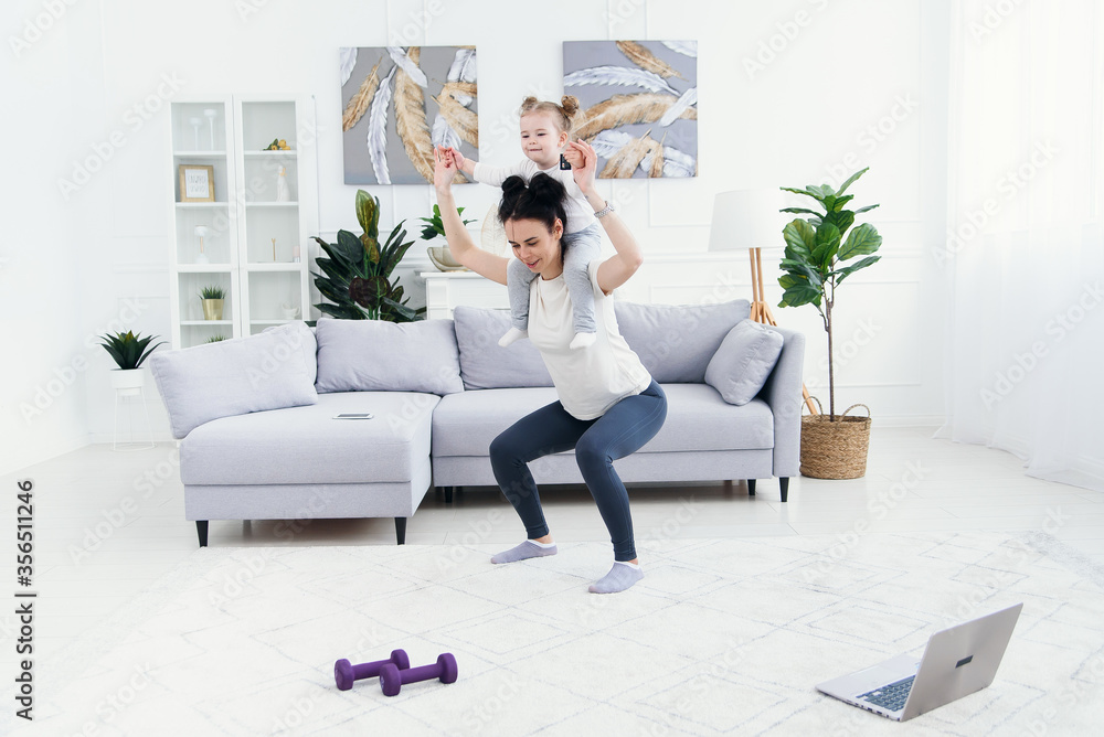 Beautiful mommy and charming little daughter are smiling while doing fitness exercises together at home. Beautiful mommy and charming little daughter are smiling while doing fitness exercises together at home.