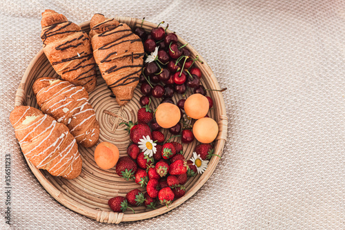 tray with croissants, strawberries, cherries and apricots on a blanket