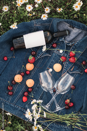 a bottle of wine, two glasses, cherries, strawberries on a denim jacket in a chamomile field