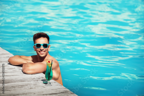 Happy young man with cocktail in swimming pool