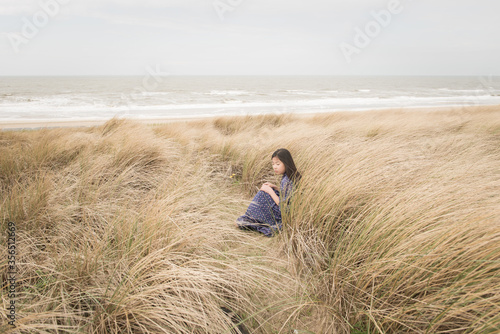 Girl in classic blue dress sitting and contemplating in grass dunes near ocean photo