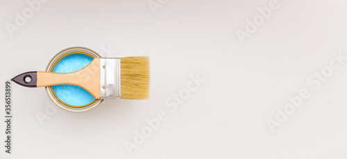 Paint brush with a wooden handle on a can of blue paint, top view. White background, free space for text.