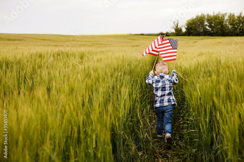 Фотография A cute blond boy is standing in a field with an American flag in his hands