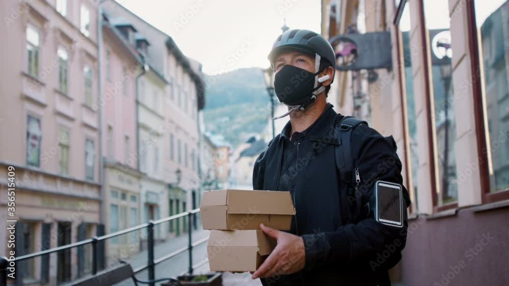 Delivery man courier with face mask delivering boxes with food in town. Delivery man courier with face mask delivering boxes with food in town.