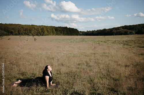 Fototapeta Naklejka Na Ścianę i Meble -  Outdoor yoga. Young overweight woman doing yoga exercise in the meadow. Open air workout, healthy lifestyle, weight loss
