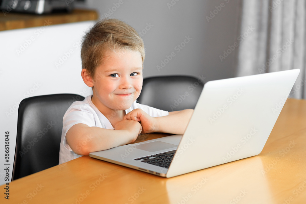 A young boy using a laptop computer sitting on top of a tableundefined at home A young boy using a laptop computer sitting on top of a tableundefined at home