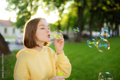 Pretty teenage girl blowing soap bubbles on a sunset. Child having fun in a park in summer.