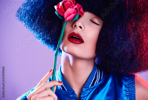 Crop female model in synthetic wig and with black lipstick showing teeth under colorful light