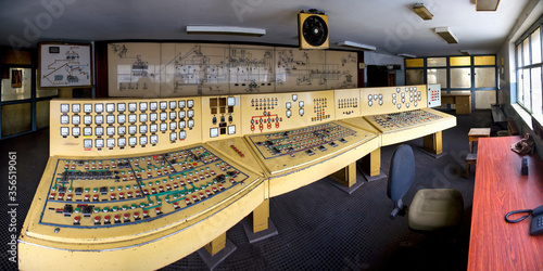 Yellow old dashboards with many buttons sensors and dials in control room with drawings and diagrams on wall in deserted building of neglect coal mine photo