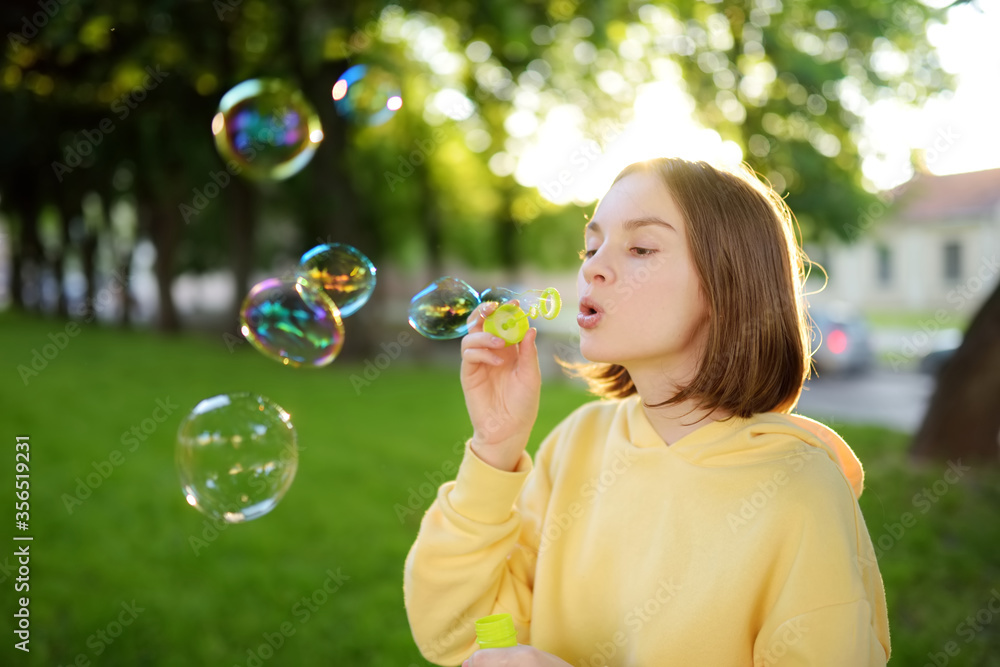Pretty teenage girl blowing soap bubbles on a sunset. Child having fun in a park in summer.