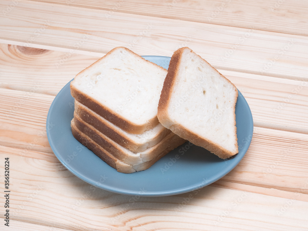 Sliced stack of bread on blue plate. Background of wooden table. Bread for sandwich. Golden slices in plate.