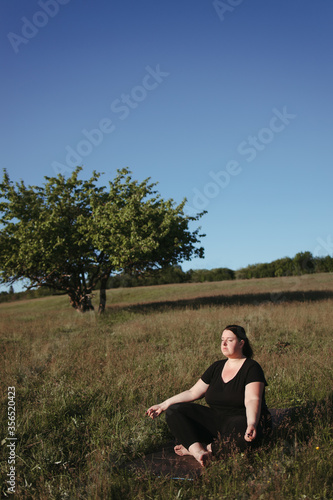 Overweight woman practicing yoga outdoors meditating sitting on fitness mat in nature. Yoga for beginners. Weight loss