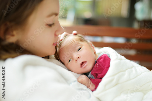 Cute big sister admiring her newborn brother. Adorable teenage girl holding her new baby boy brother. Kids with large age gap. Big age difference between siblings.