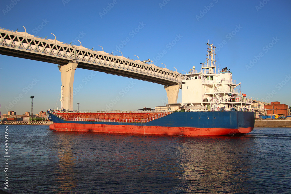 container cargo ship navigates a canal under a high-speed highway bridge
