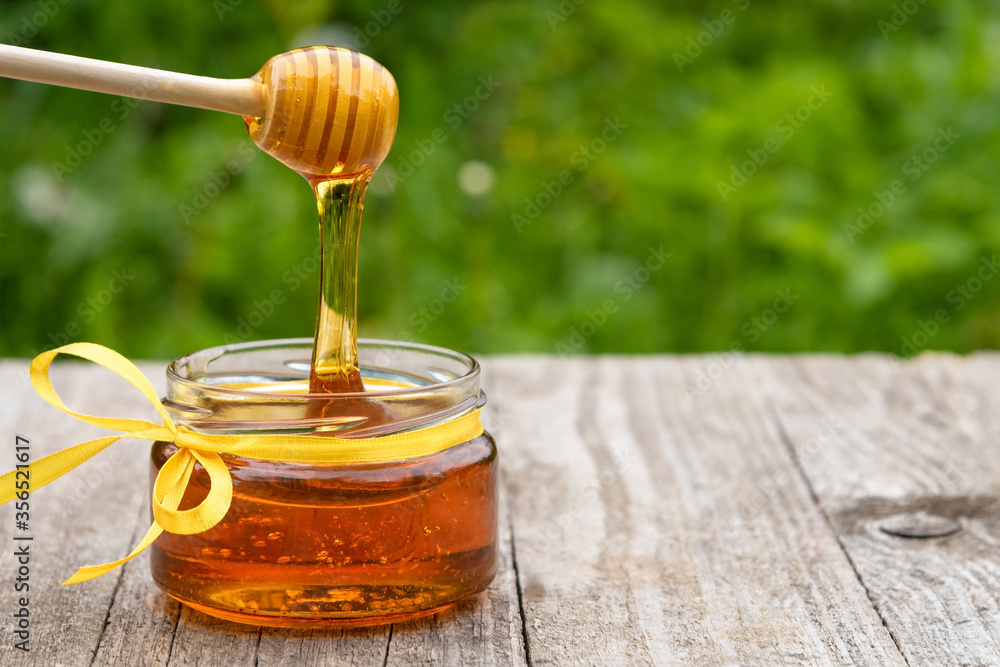 Dripping honey from a wooden spoon on a grassy green background with copy space. Dripping honey from a wooden spoon on a grassy green background with copy space.