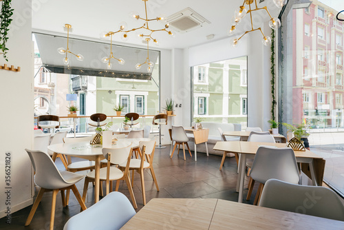 Interior of spacious light contemporary restaurant with big windows decorated with exotic plants and cozy chairs at tables under creative pendant lamps photo
