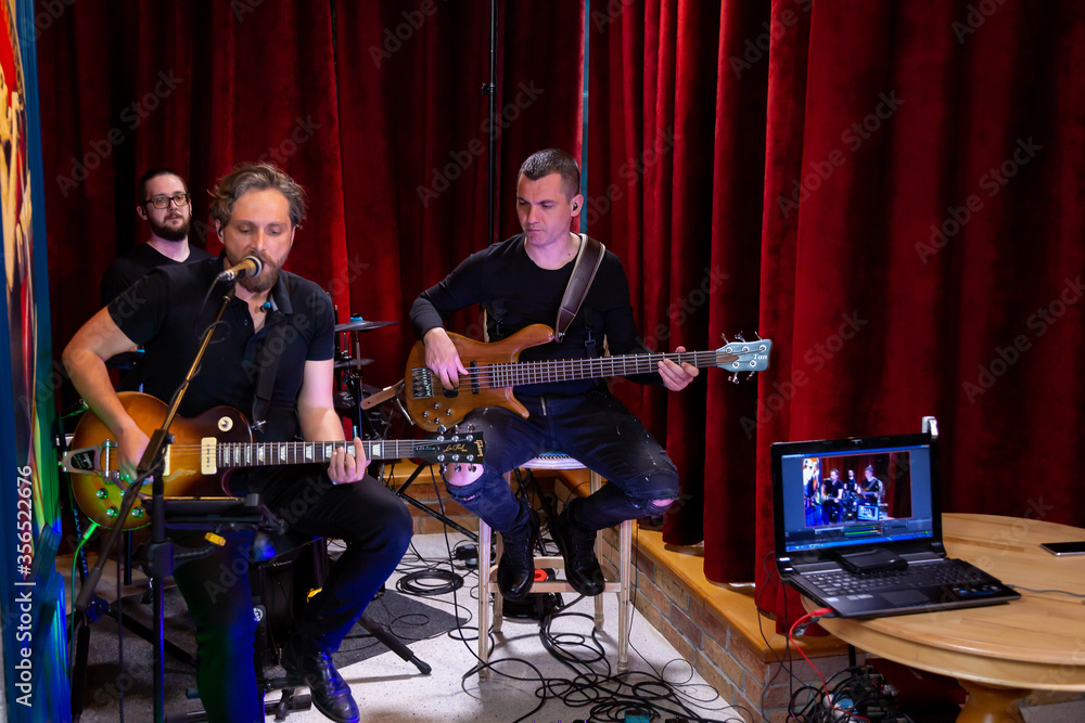 Fototapeta The band of Musicians playing Electric Guitar, Bass Guitar and Drums during the Concert Broadcast Online on social media platforms in the Bar. isolated on a red background.