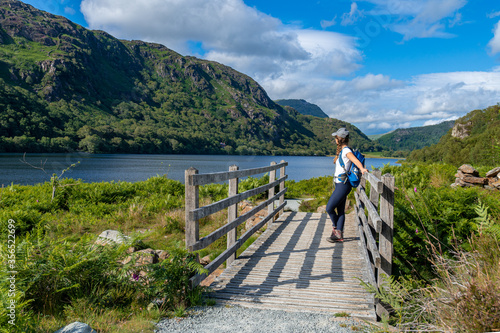 A solo female hiker resting on a bridge while looking at the amazing view of the lake and hills in Snowdonia National Park in Wales 