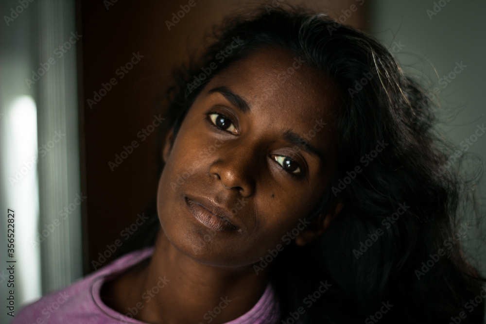 Attractive young ethnic lady with long wavy hair wearing trendy pink clothes standing in modern room with hands on waist and looking at camera thoughtfully Attractive young ethnic lady with long wavy hair wearing trendy pink clothes standing in modern room with hands on waist and looking at camera thoughtfully
