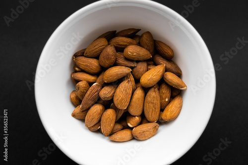 Almonds in a small plate on a black table. Almond is a healthy vegetarian protein nutritious food. Natural nuts snacks.