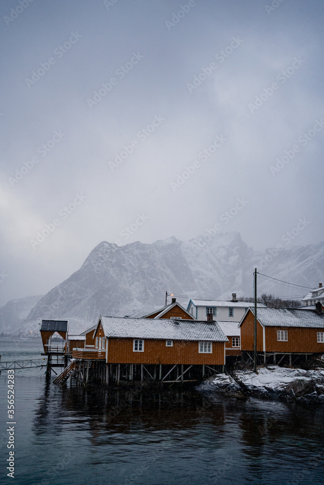 Yellow country houses on coast of strait against misty snowy mountain crests in overcast weather in Norway Yellow country houses on coast of strait against misty snowy mountain crests in overcast weather in Norway