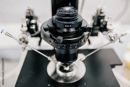 Lens of modern machine over Petri dish and manipulators during process of ovum fertilization in contemporary lab of clinic photo