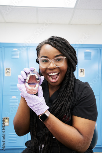 Happy black dental technician with braids looking at camera and showing false teeth while working in contemporary laboratory
