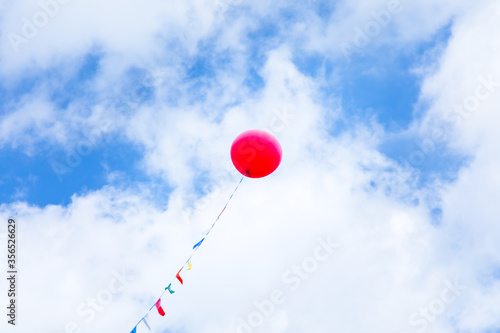 Red helium balloon high in the blue sky with clouds