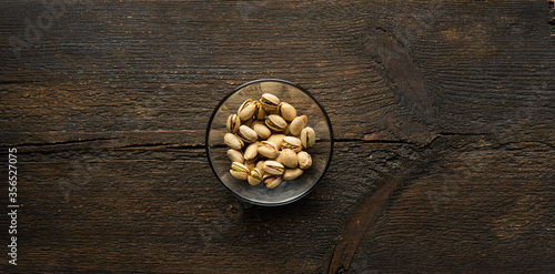 Pistachios in a small plate on a vintage wooden table. Pistachio is a healthy vegetarian protein nutritious food. Natural nuts snacks.