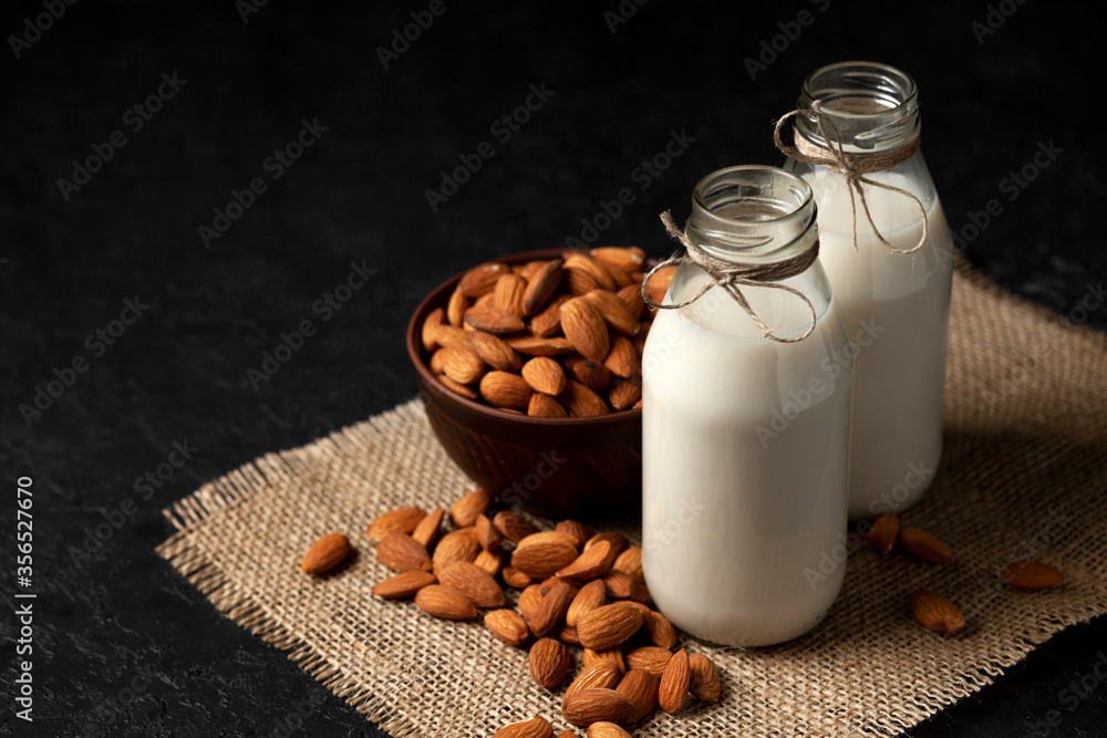 almond milk in bottles with nuts on a dark black table, a variety of dairy products without sugar and lactose, a vegetarian drink almond milk in bottles with nuts on a dark black table, a variety of dairy products without sugar and lactose, a vegetarian drink
