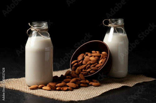 two bottles of almond milk with nuts on a dark black table  vegetarian milk without sugar and lactose