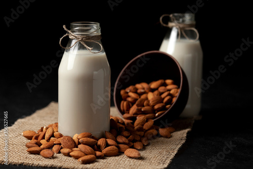 two bottles of almond milk with nuts on a dark black table  vegetarian milk without sugar and lactose