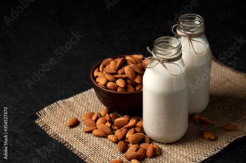 almond milk in bottles with nuts on a dark black table  a variety of dairy products without sugar and lactose  a vegetarian drink