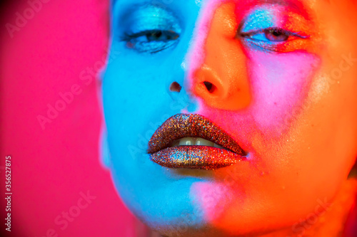 Fashion model metallic silver lips and face woman in neon uv blue and purple lights, posing in studio, beautiful girl, glowing make-up, colorful make up. 