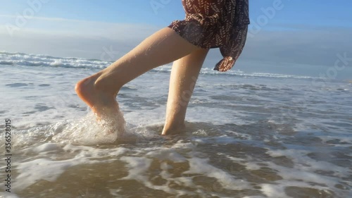 feet come out of ocean close-up, girl in dress walks on tsand comes out of water slow motion photo