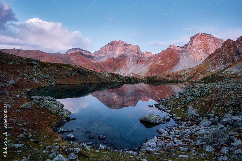 Beautiful mountains at sunset in clouds, gold alpine field, lakes and mountain ranges, travel and mountain life. Campground by the lake