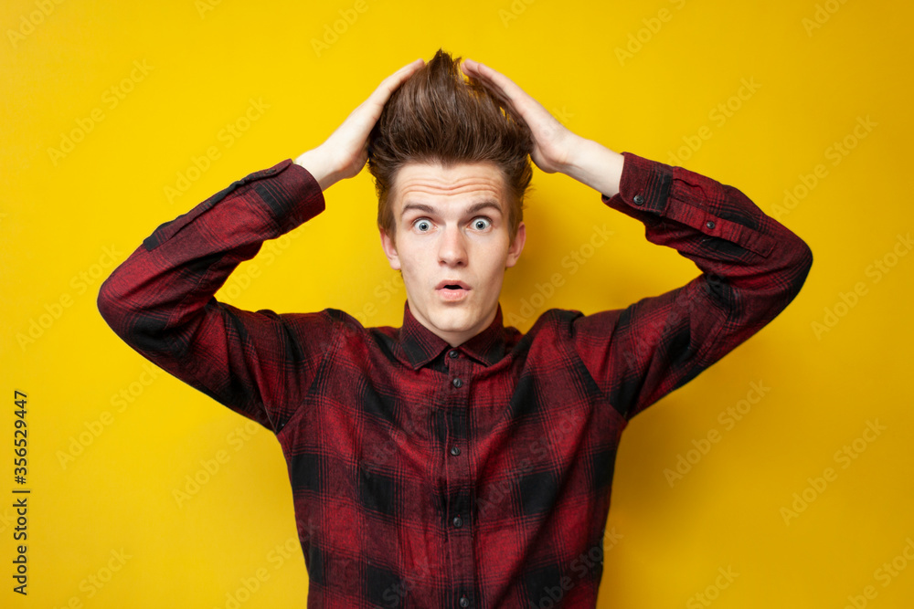 shocked guy touches his hair and wonder at yellow isolated background, hipster student with strong styling shows a haircut shocked guy touches his hair and wonder at yellow isolated background, hipster student with strong styling shows a haircut