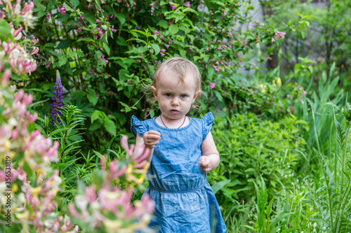 Beautiful little cute blond girl sniffing flowers in the garden.