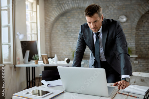 Serious businessman reading e-mail on laptop in the office. © Drazen