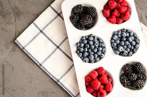 Fresh berry raspberries, blueberries and blackberries in white iron baking, with a napkin on a gray concrete background. photo